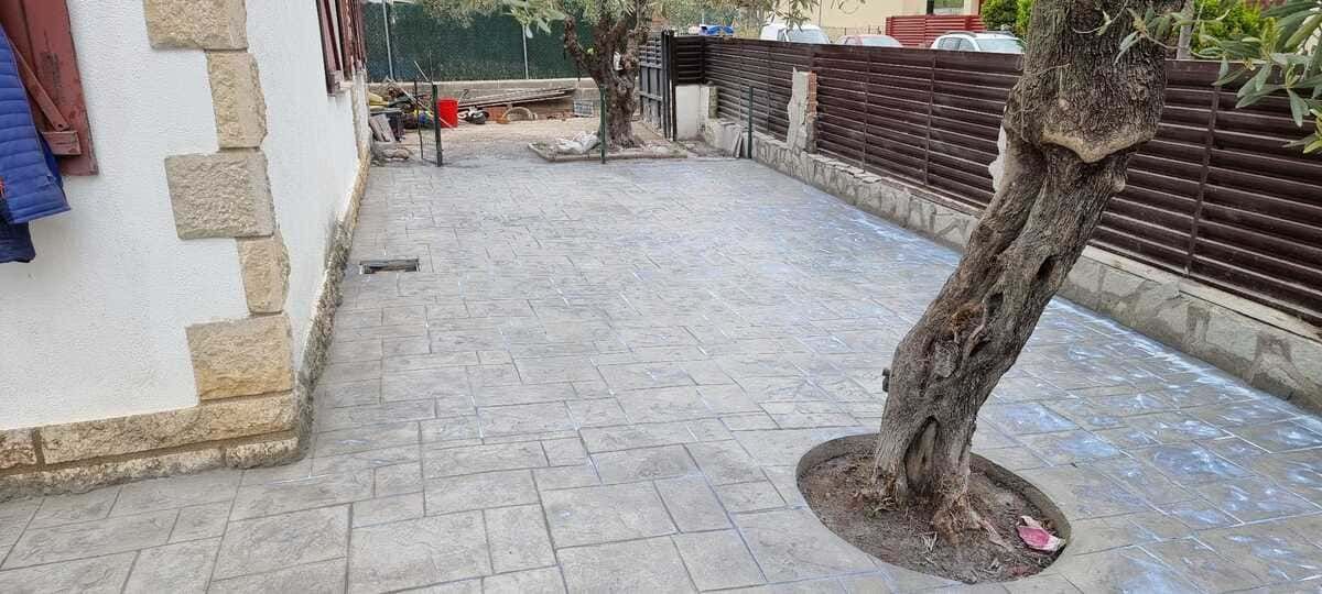 Un patio exterior pavimentado con un gran tronco de árbol a la derecha y un edificio a la izquierda.