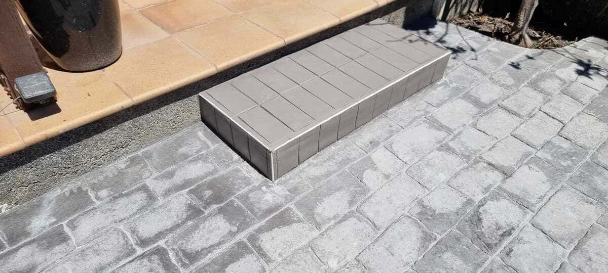 Un pequeño escalón de ladrillo gris en un patio de piedra al lado de un borde de baldosas de color marrón.
