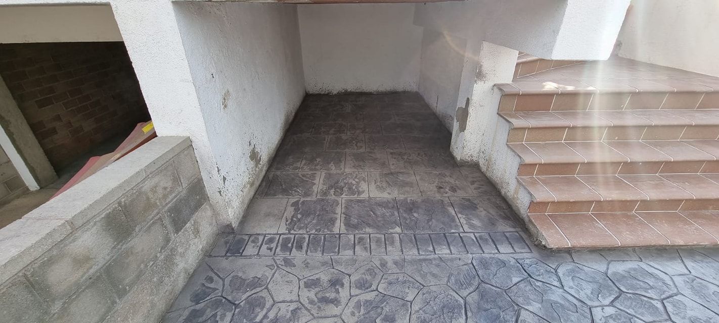 Escaleras de hormigón que conducen a una pasarela cubierta con baldosas estampadas y paredes desgastadas.