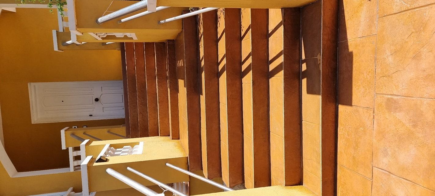 Superficie de hormigón gris recién vertido en un entorno exterior, con edificios al fondo.