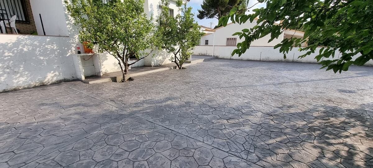 Una zona pavimentada vacía con tres árboles pequeños y edificios blancos.