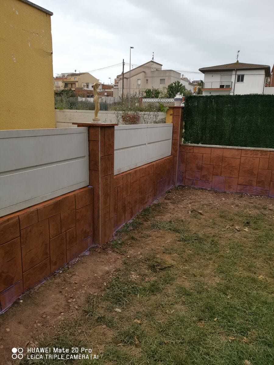 Una valla de hormigón de color marrón y gris rodea un patio con césped.