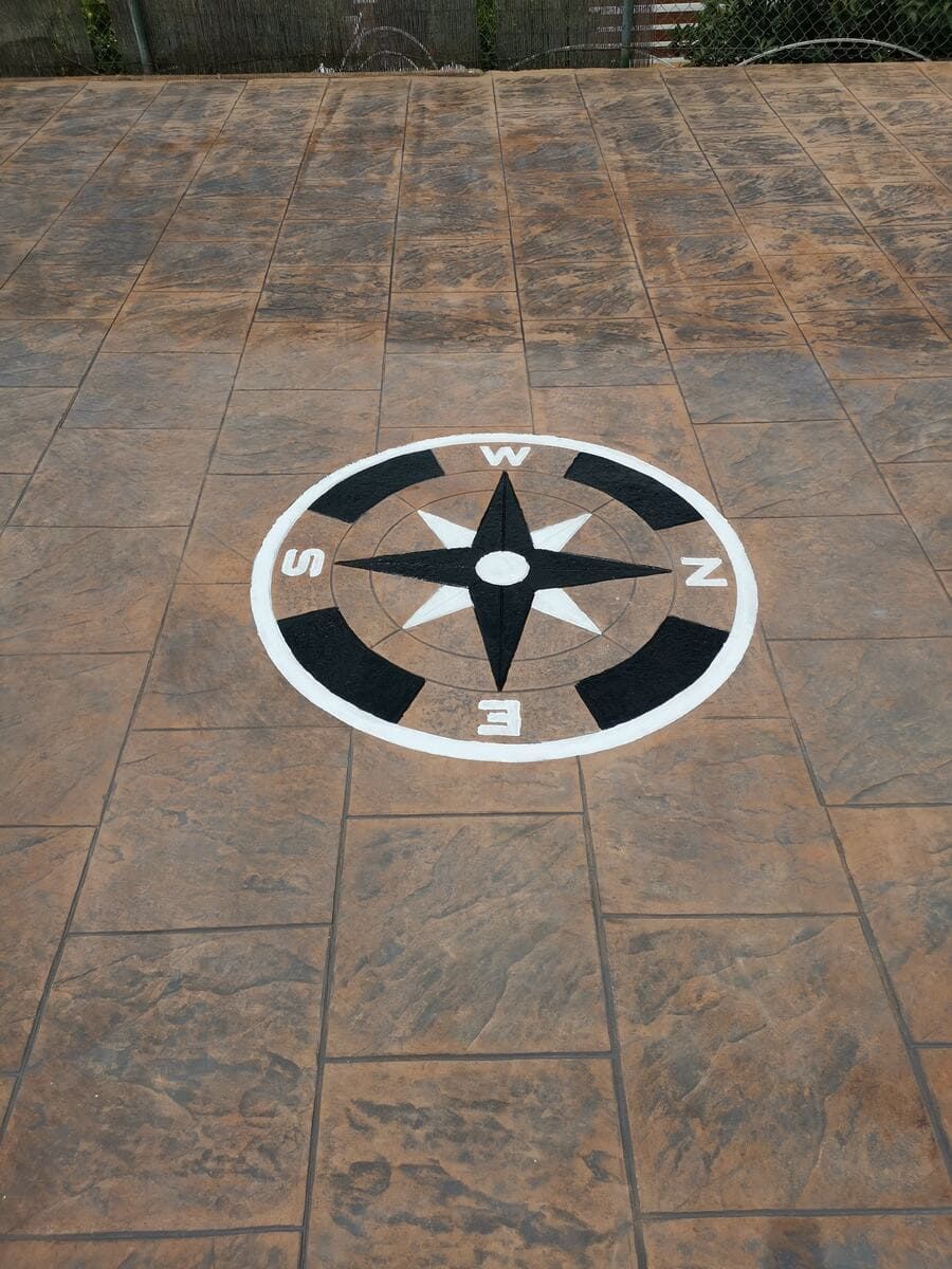 Diseño de rosa de los vientos sobre un patio de baldosas marrones. Se ven marcadores direccionales en blanco y negro.