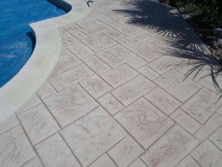 Patio de hormigón estampado que rodea una piscina, color tostado, patrón geométrico texturizado.