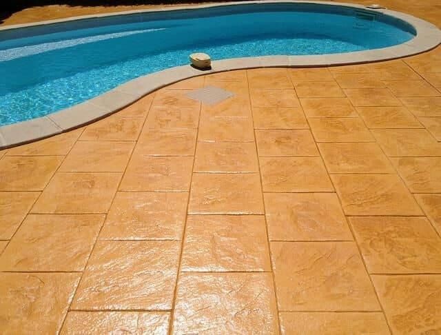 Patio junto a la piscina con hormigón estampado, junto a una piscina azul. Colores cálidos en tonos tierra.