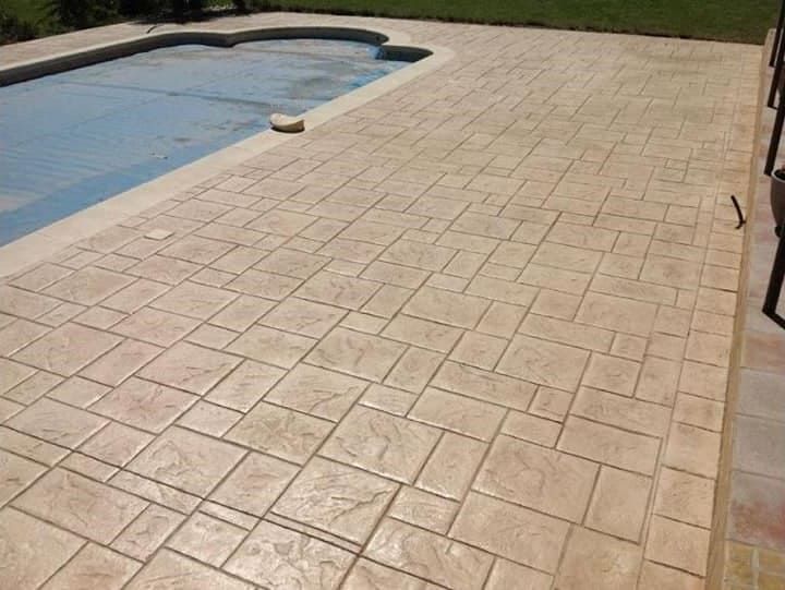 Patio de hormigón estampado que rodea una piscina, color tostado, patrón de baldosas cuadradas.