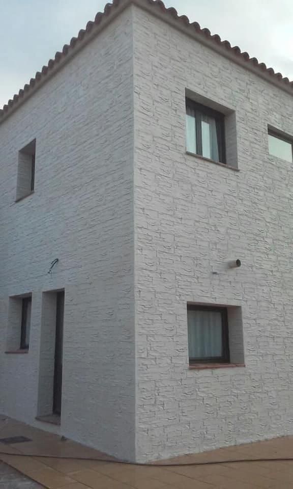 Edificio de dos pisos de estuco blanco con ventanas de marco oscuro y techo de tejas rojas en una esquina.