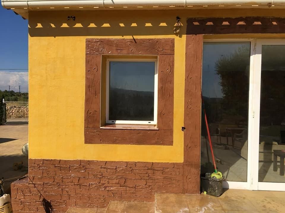 Exterior de edificio de color amarillo con marco y base de ventana de piedra marrón y puerta corrediza de vidrio blanca.
