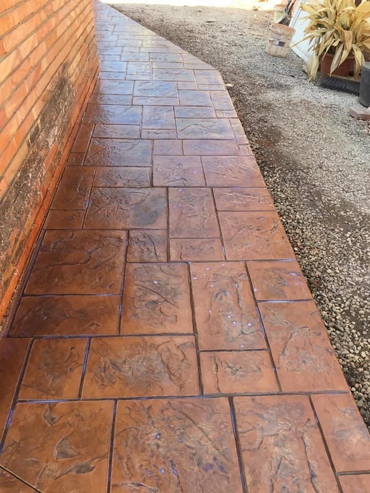 Pasarela de hormigón estampado de color marrón junto a un muro de ladrillo y grava.