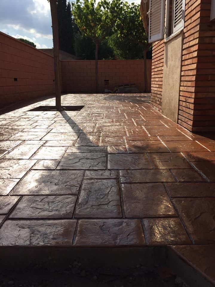 Patio de hormigón estampado en un entorno revestido de ladrillo, que muestra patrones rectangulares y cuadrados y un color marrón oscuro.