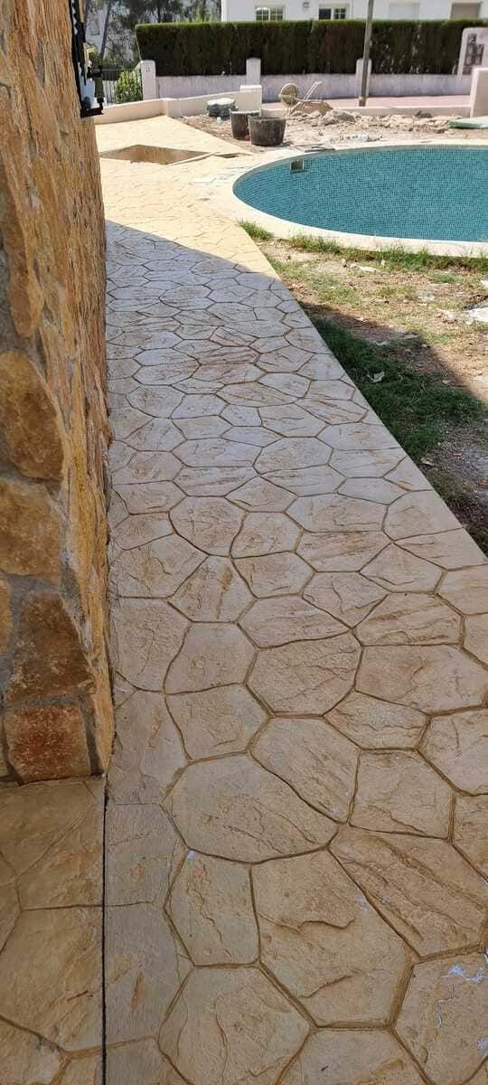 Pasarela con dibujos de piedra junto a una piscina, al lado de un muro de piedra.