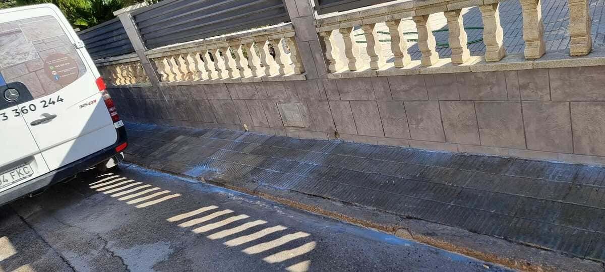 Una furgoneta blanca estacionada junto a un muro bajo de piedra con una balaustrada ornamentada. Carretera sombreada.