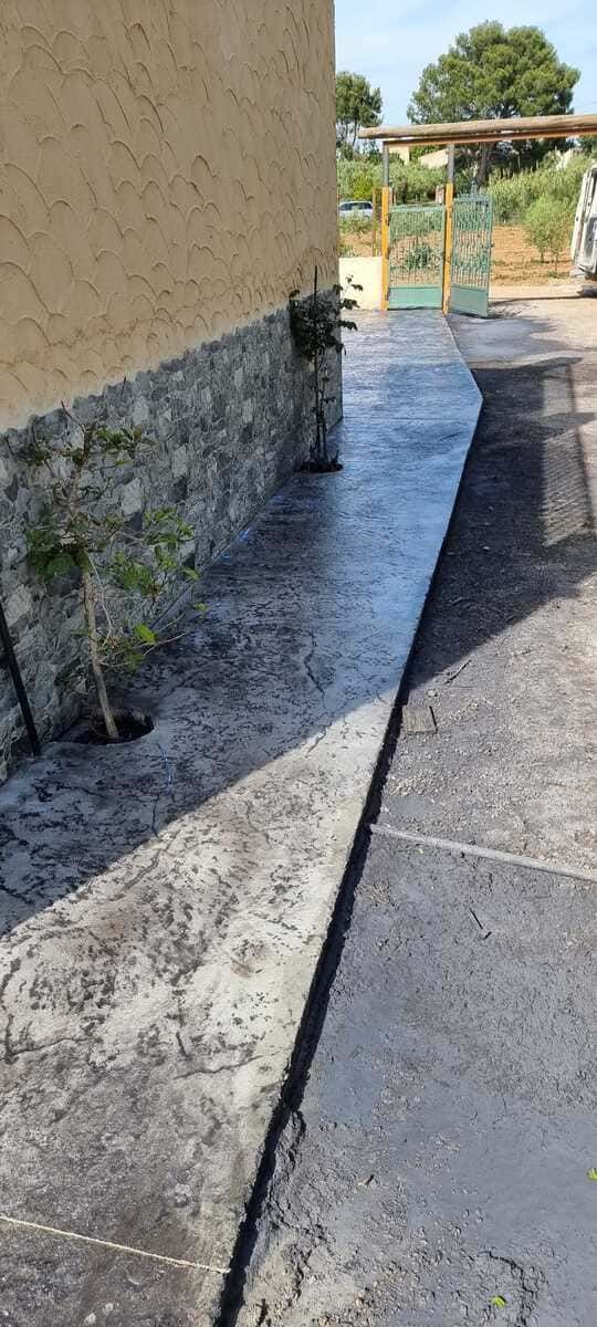 La acera junto a un edificio con una pared de piedra texturizada conduce a una puerta abierta.