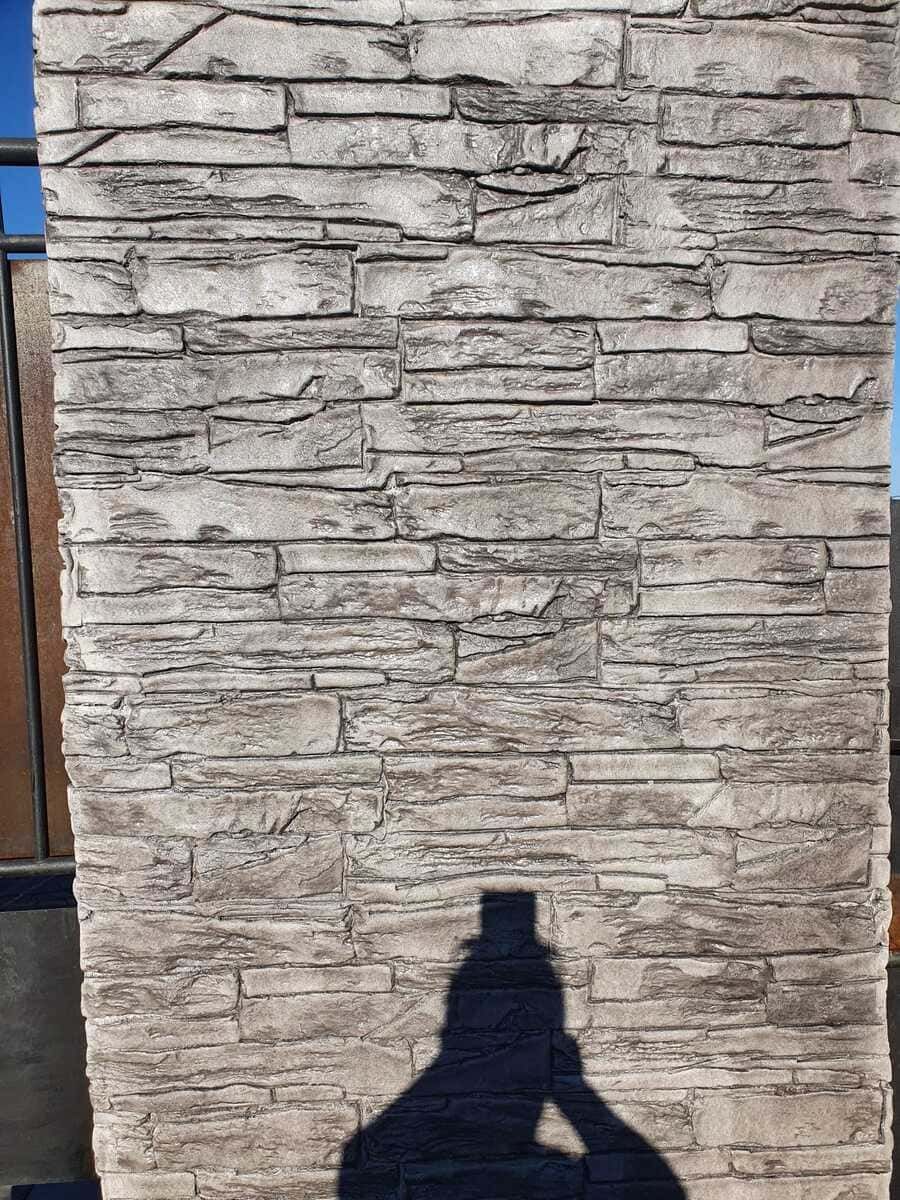 Fachada de piedra en tonos gris claro con sombra de persona.