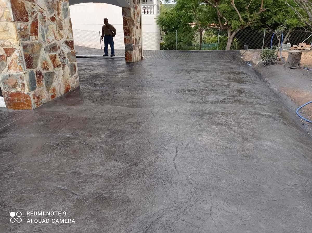 Camino de hormigón que conduce a un arco de piedra con una persona parada en el interior.