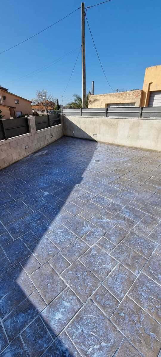 Un patio pavimentado con patrón de bloques de hormigón, bordeado por muros bajos y un cielo azul.