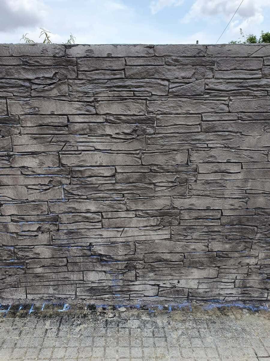 Muro de ladrillos de piedra gris con un suelo pavimentado debajo y un cielo parcialmente nublado arriba.