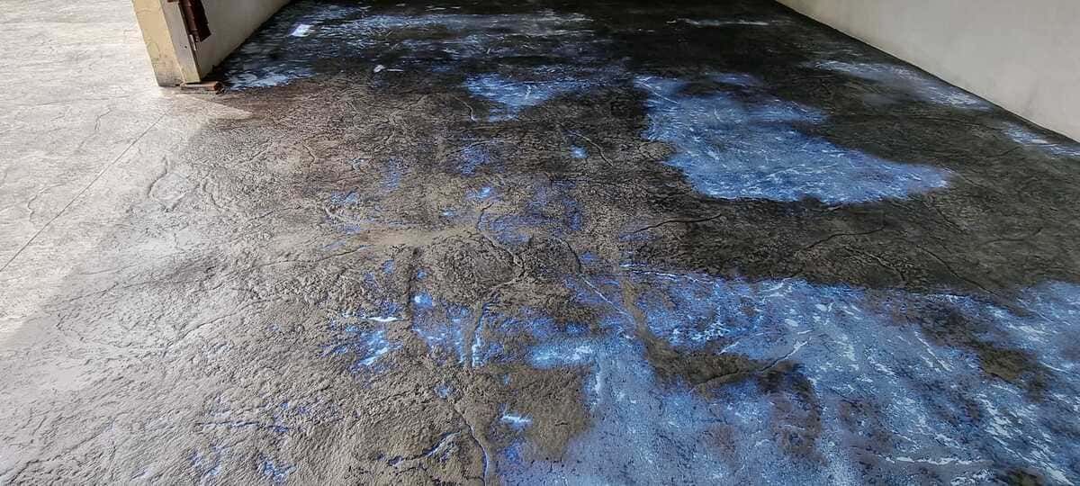 Superficie de hormigón con manchas azules. Se ve el marco de una puerta a la izquierda.