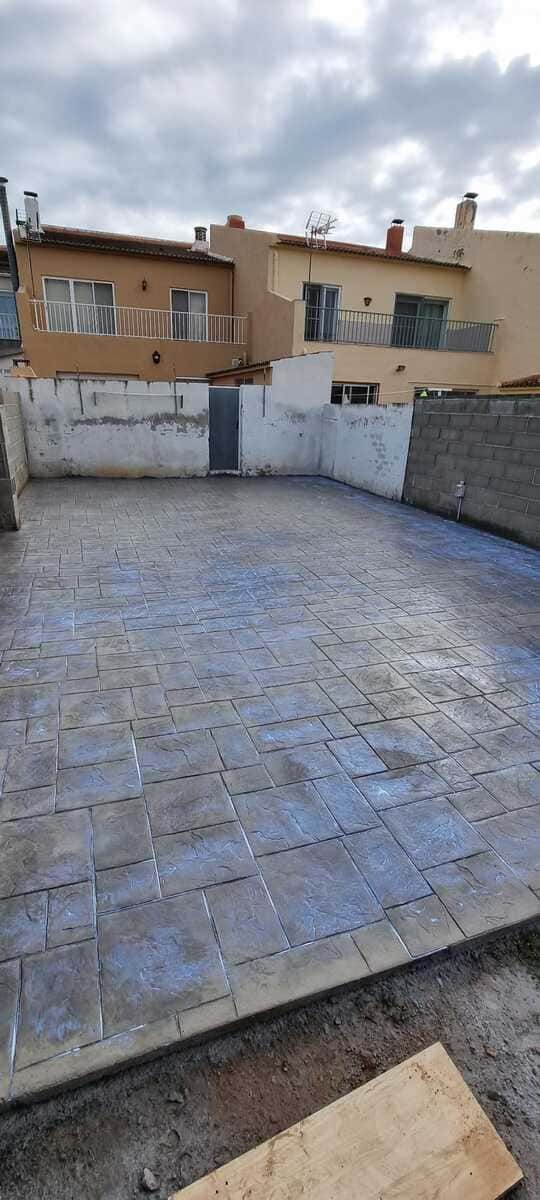 Patio de hormigón estampado recién colocado con edificios al fondo bajo un cielo nublado.