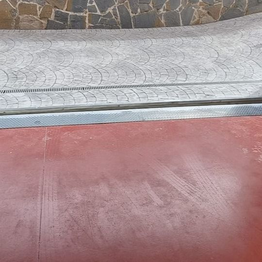 Superficie roja con huellas de neumáticos, borde plateado y pasarela gris estampada.