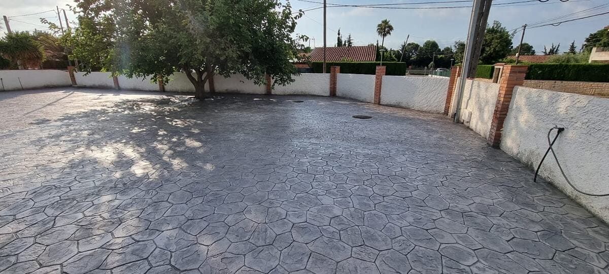 Vista de un patio pavimentado rodeado por una pared blanca con pilares de ladrillo y un gran árbol en el centro.