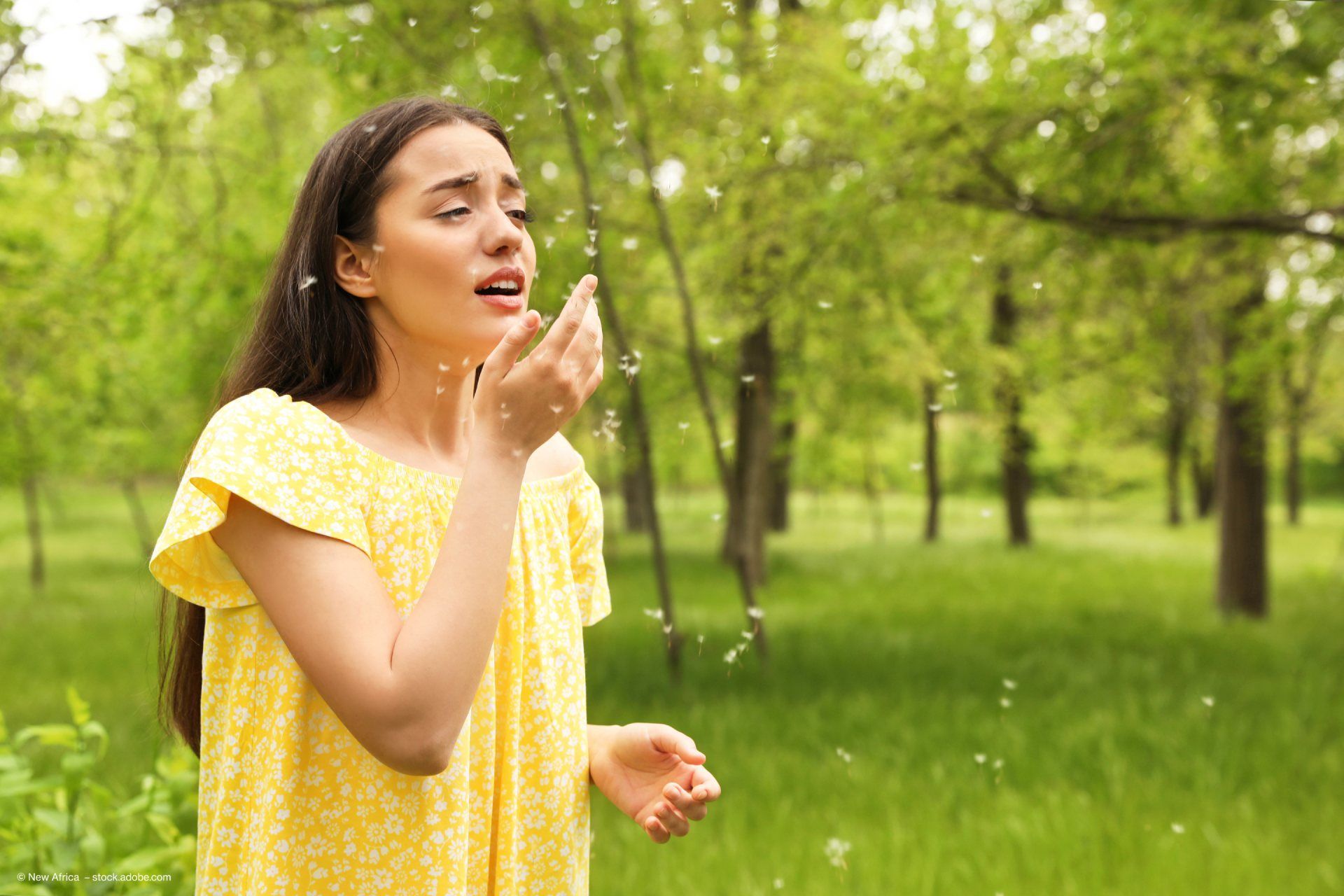 Frau niest auf einer Wiese mit Pollen vorm Gesicht