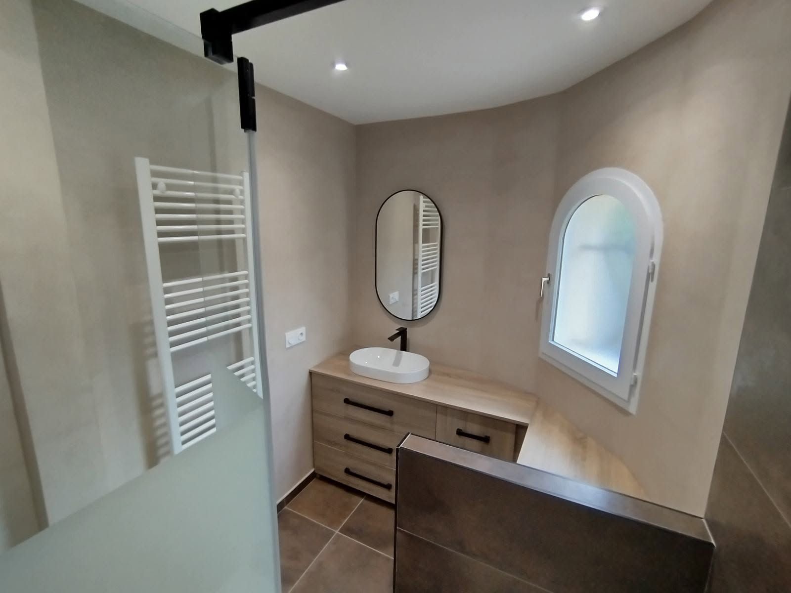 Salle de bains moderne avec une douche à l'italienne, un meuble de lavabo, un miroir et une petite fenêtre cintrée