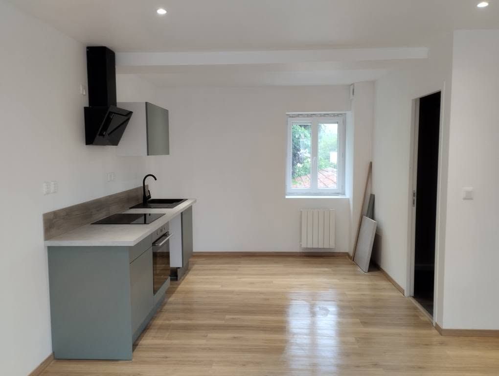 Cuisine moderne vide avec du parquet clair, des placards gris, une hotte noire et une fenêtre.