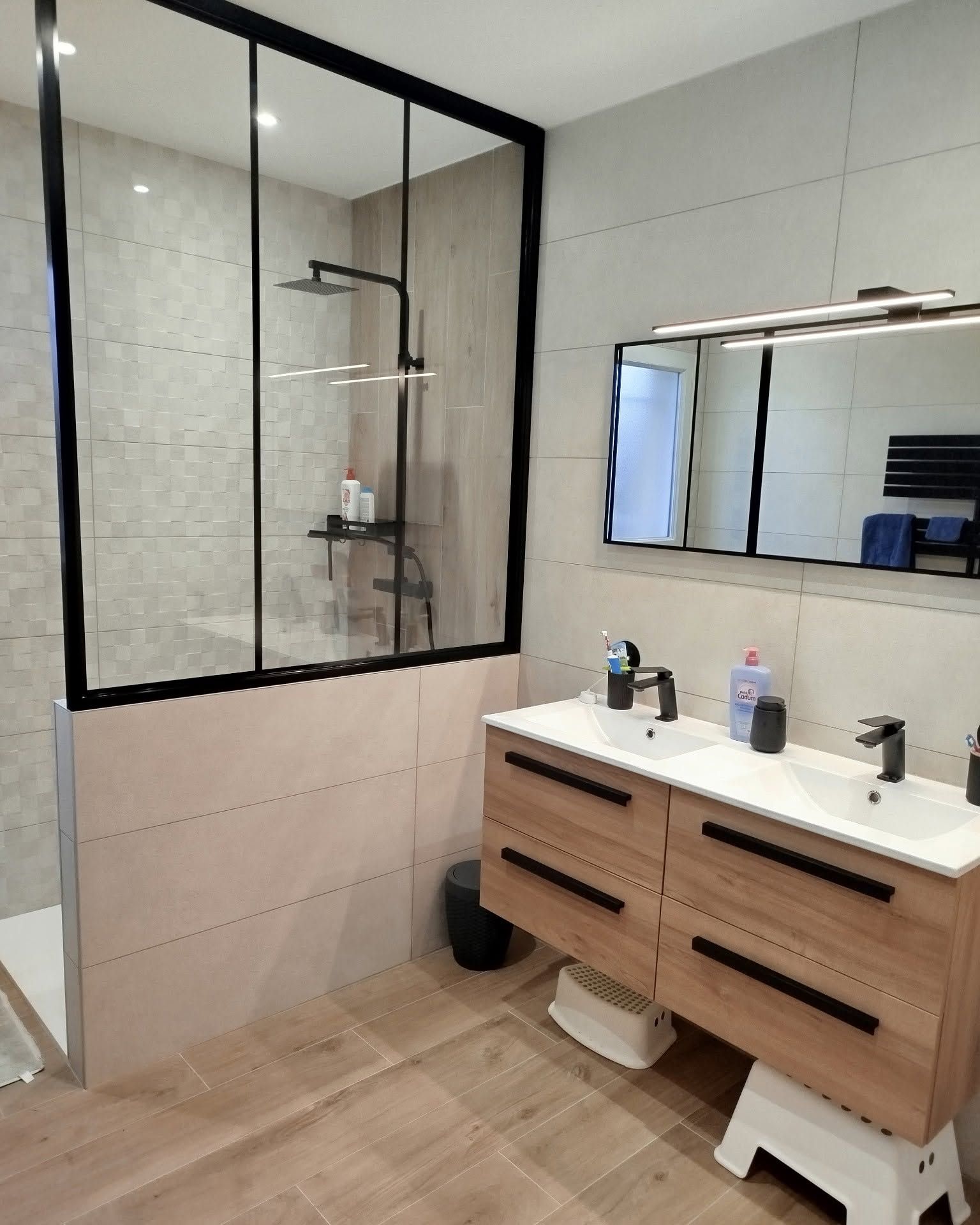 Salle de bains moderne avec une douche en verre, un grand miroir et un meuble de lavabo en bois avec une double vasque.