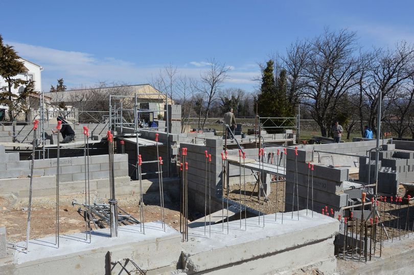 Chantier de construction avec des fondations en béton, des armatures et des ouvriers sous un ciel dégagé