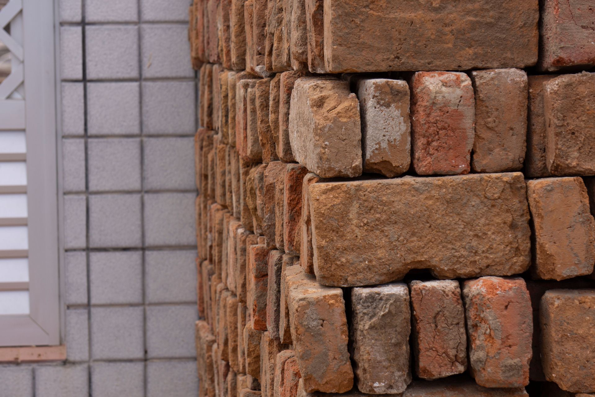 Briques beiges empilées à côté d'un mur carrelé gris clair et d'une fenêtre à cadre blanc