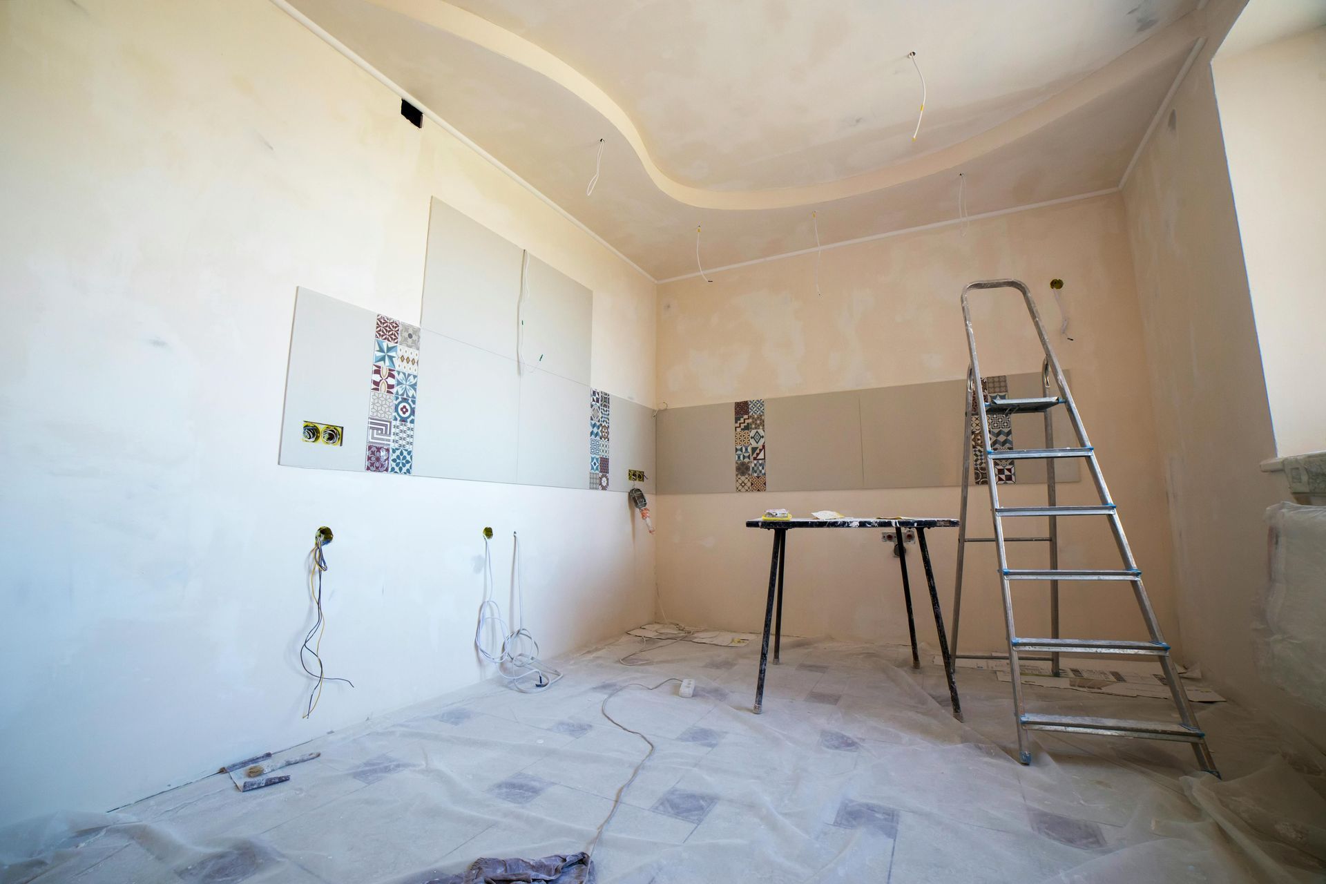 Pièce partiellement rénovée avec des murs plâtrés, une échelle et une table de travail sur un sol recouvert