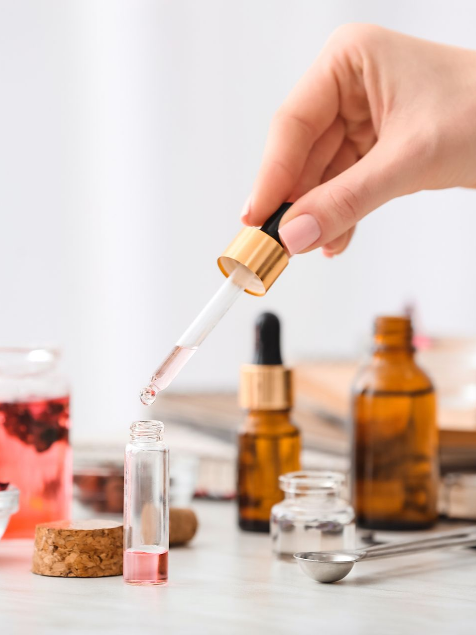 Main tenant un compte-gouttes versant du liquide dans un flacon ; flacons posés sur une surface blanche.