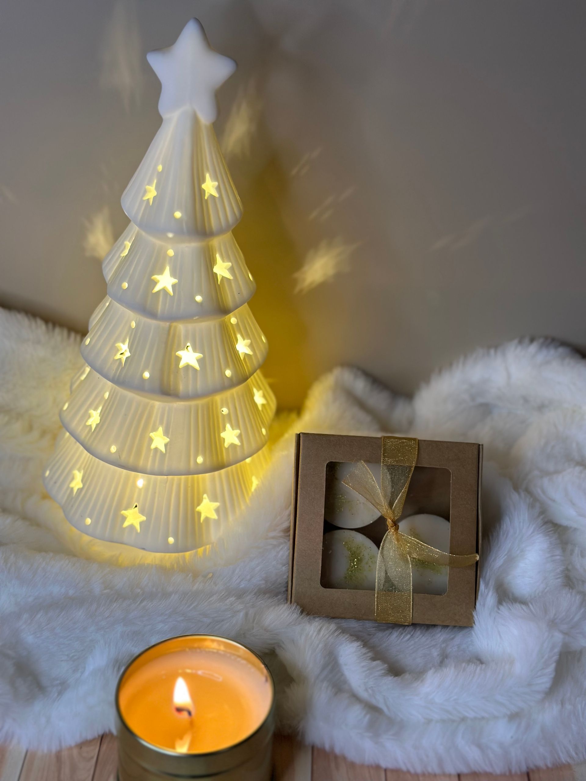 Sapin de Noël en céramique illuminé et bougies sur une surface blanche et moelleuse.