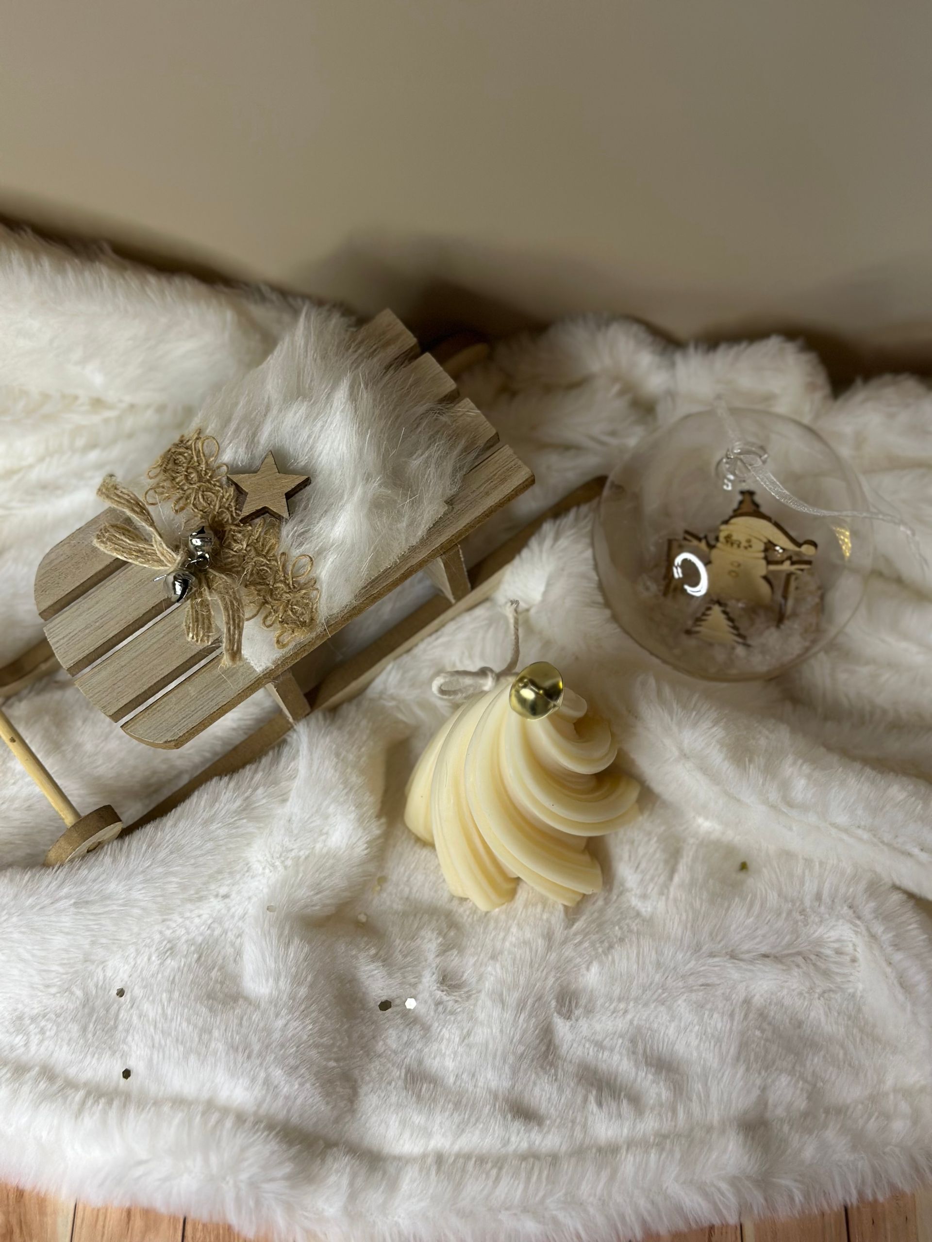 Décorations de Noël sur une surface en fausse fourrure blanche : traîneau, sapin en spirale, globe transparent avec scène miniature.
