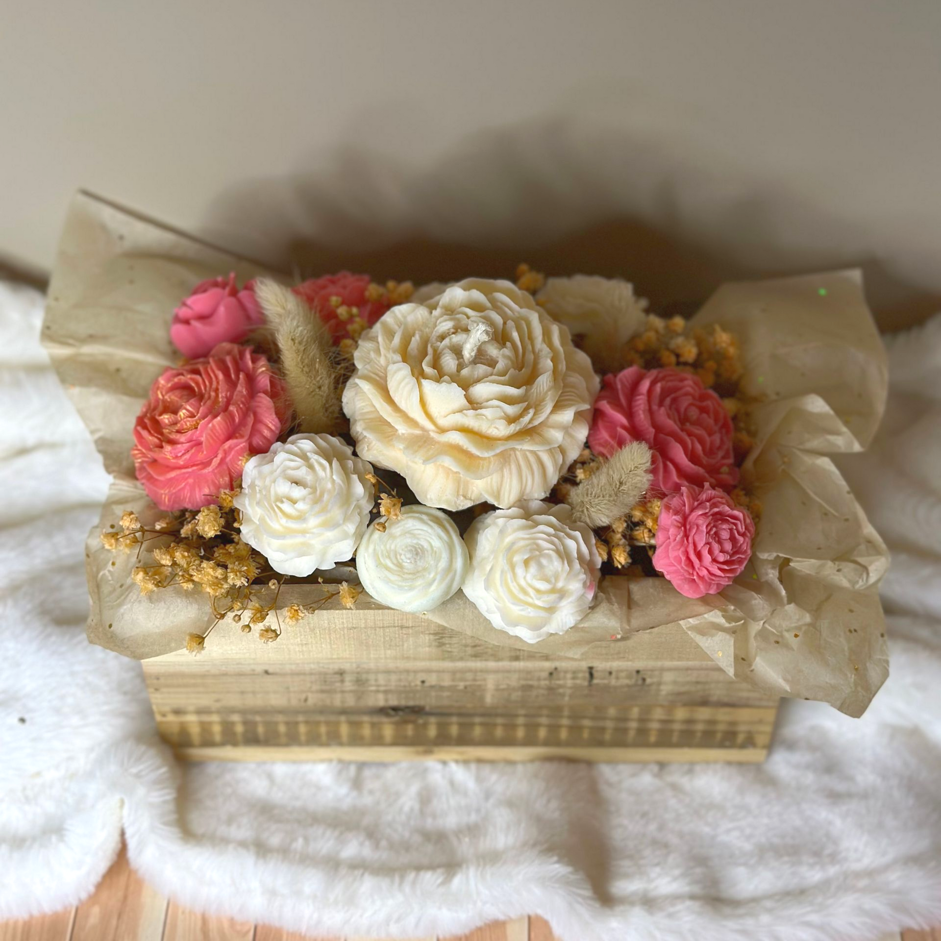Composition florale de bougie en boîte de bois avec des fleurs crème, roses et pêche, emballée dans du papier kraft.