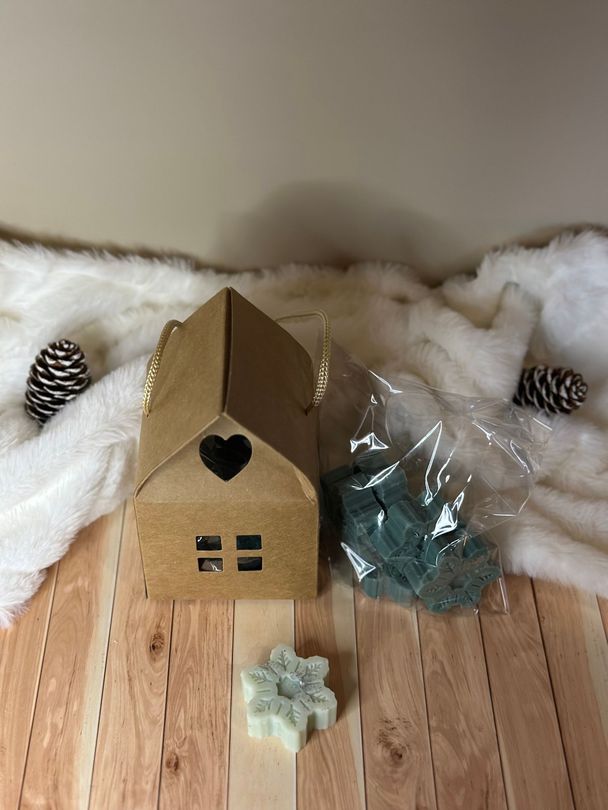 Une petite maison brune avec une découpe en forme de cœur et des fondants de cire verte sur une surface en bois avec une couverture en fourrure blanche.