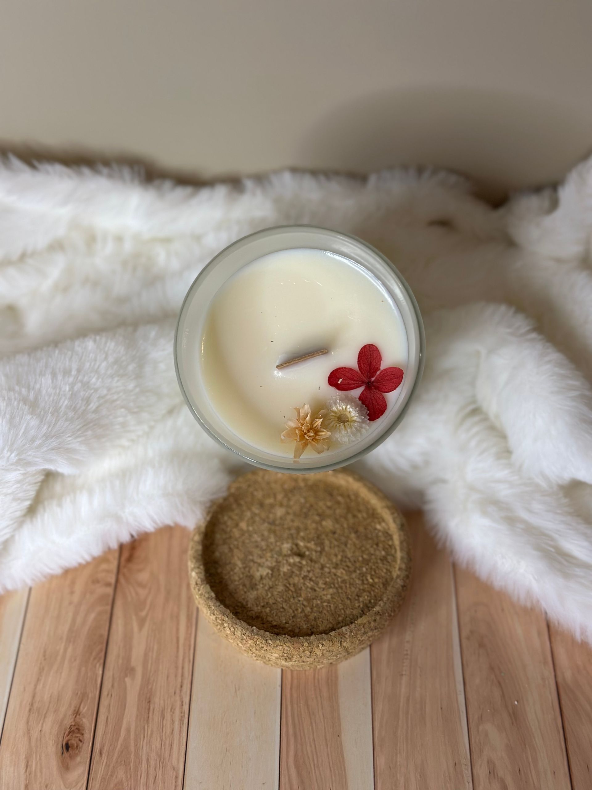 Trois bougies crème disposées en spirale et des pommes de pin sur un plateau en bois, détail de corde, sur un mur blanc.