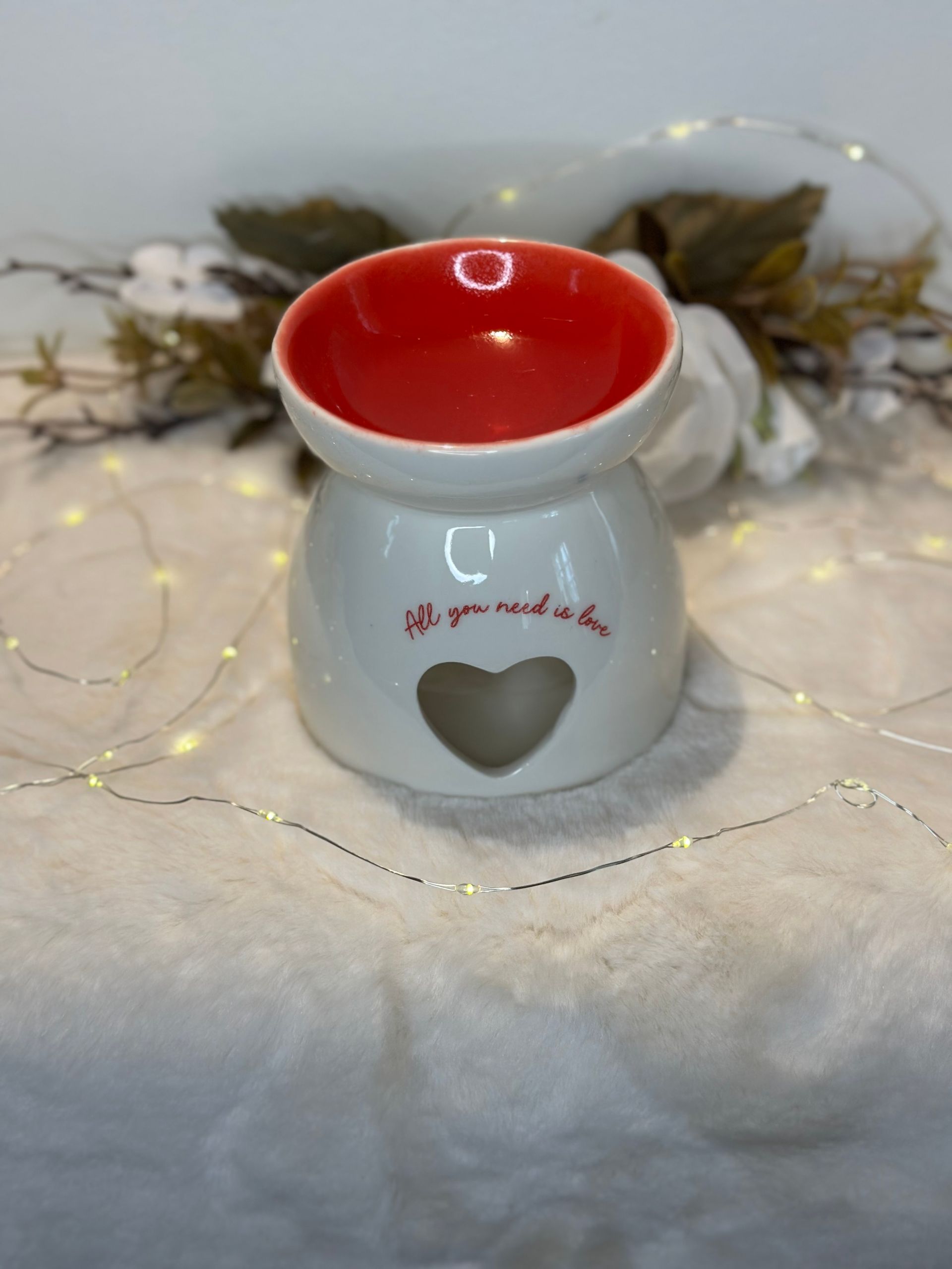 Chauffe-huile en céramique blanche en forme de maison, avec des fenêtres lumineuses sur une surface enneigée.