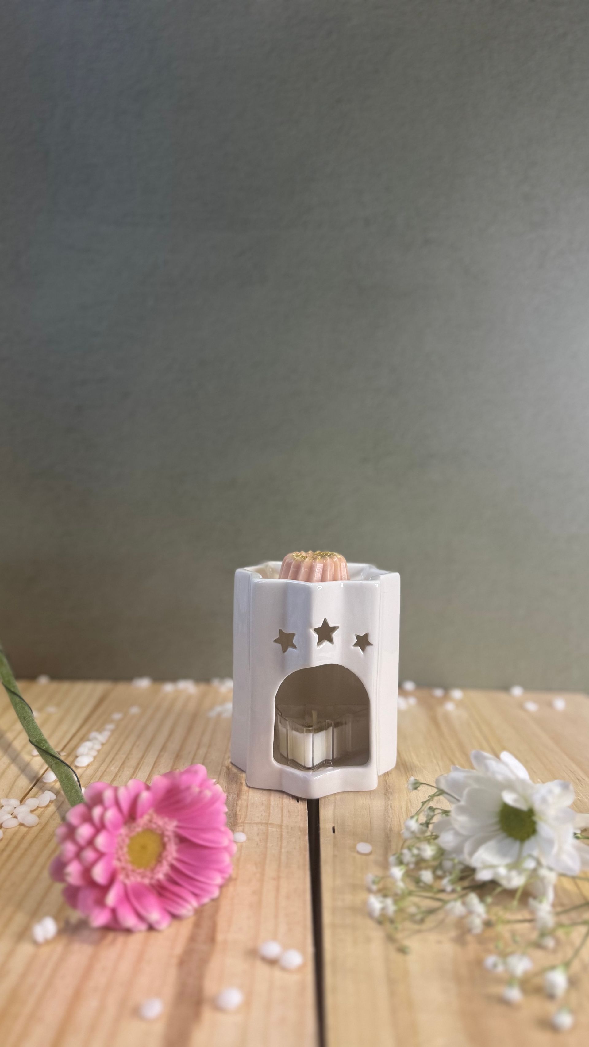 Chauffe-cire en céramique blanche avec découpe « maison », illuminé, et contient une cire verte fondante. Posé sur un tapis blanc moelleux.