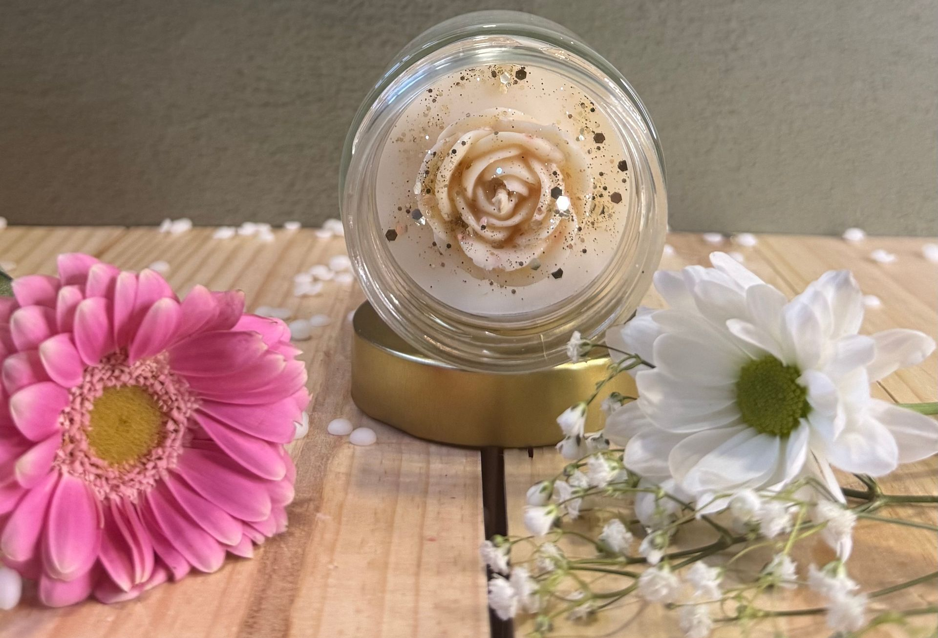 Bougie dorée allumée, avec en arrière-plan un arrangement floral flou de fleurs roses et orange.