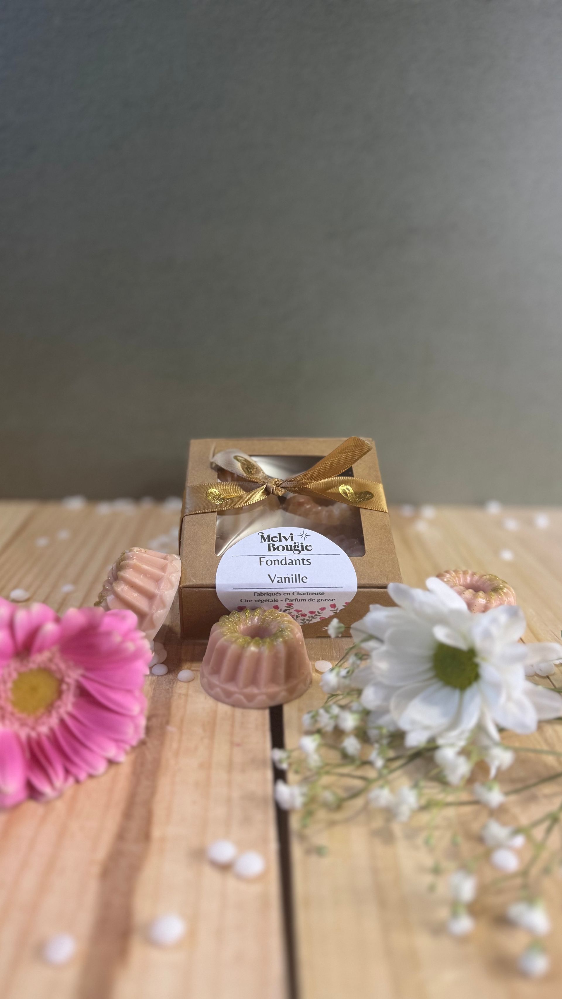 De petits fondants en forme de fleur, dans des sachets transparents fermés par un ruban, sont posés sur de la dentelle, à côté d'une bougie.