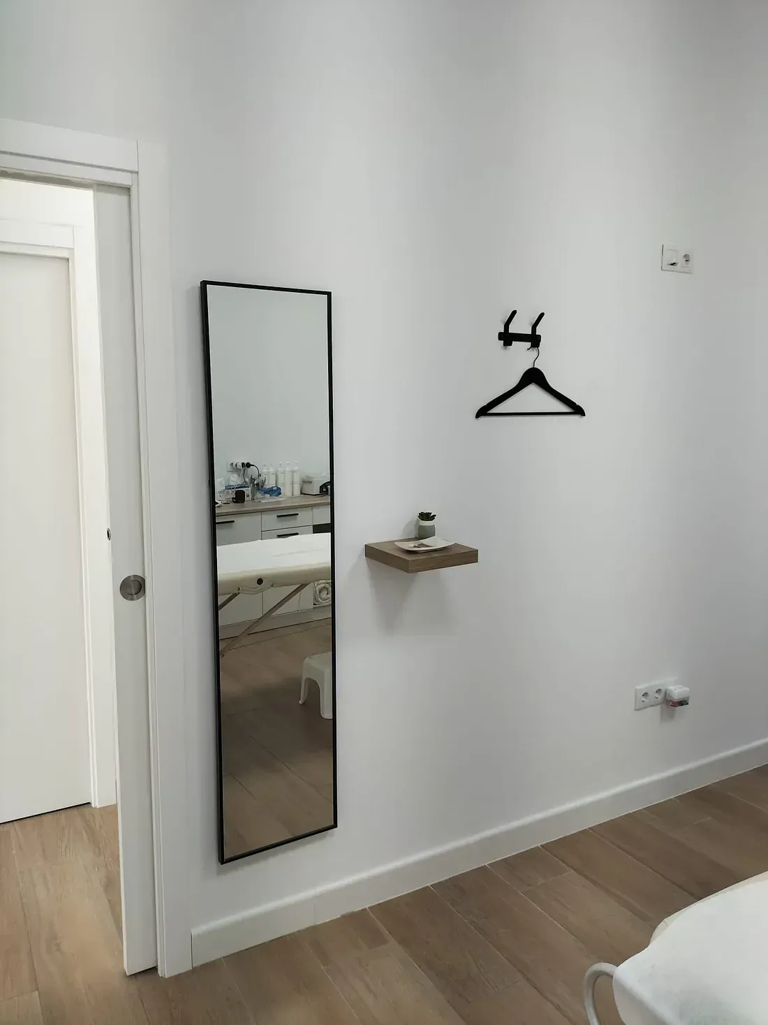 Un espejo de cuerpo entero está colgado en una pared blanca al lado de una percha.