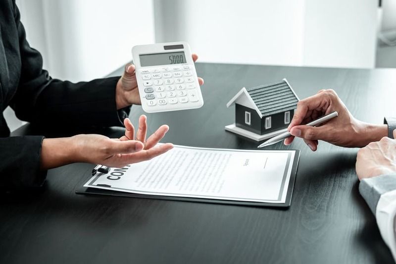 Una mujer sostiene una calculadora al lado de una casa modelo.