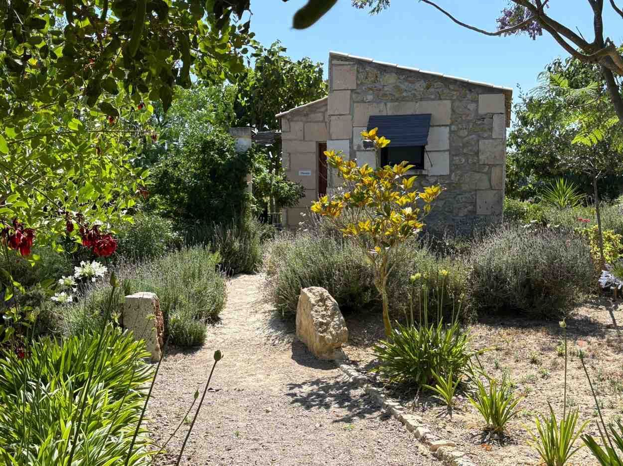 Casa rural de piedra con techo naranja junto a campos y árboles bajo un cielo azul.