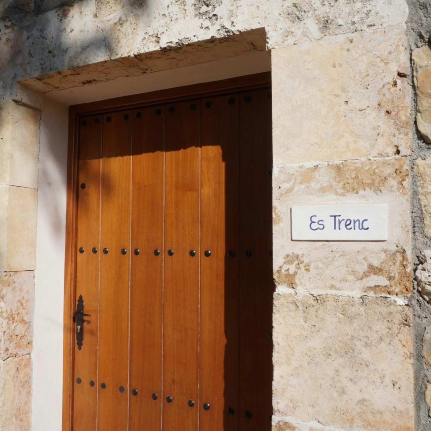 Puerta de madera en un muro de piedra con un pequeño letrero que dice “Es Trenc”.