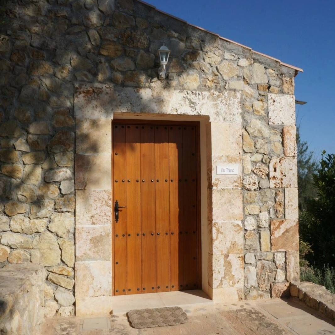 Fachada de piedra con puerta de madera y pequeños escalones bañados por la luz del sol.