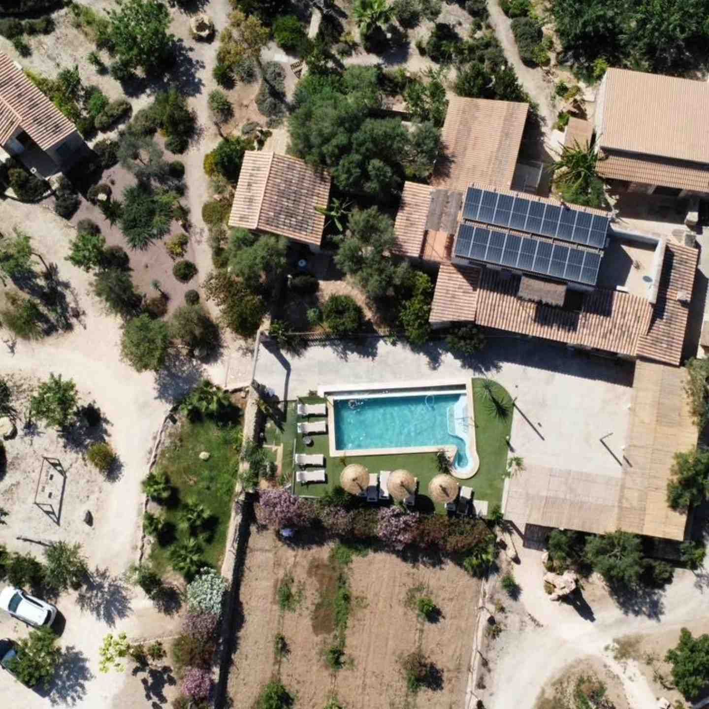 Vista aérea de una casa rural con piscina, jardín y paneles solares rodeada de árboles.