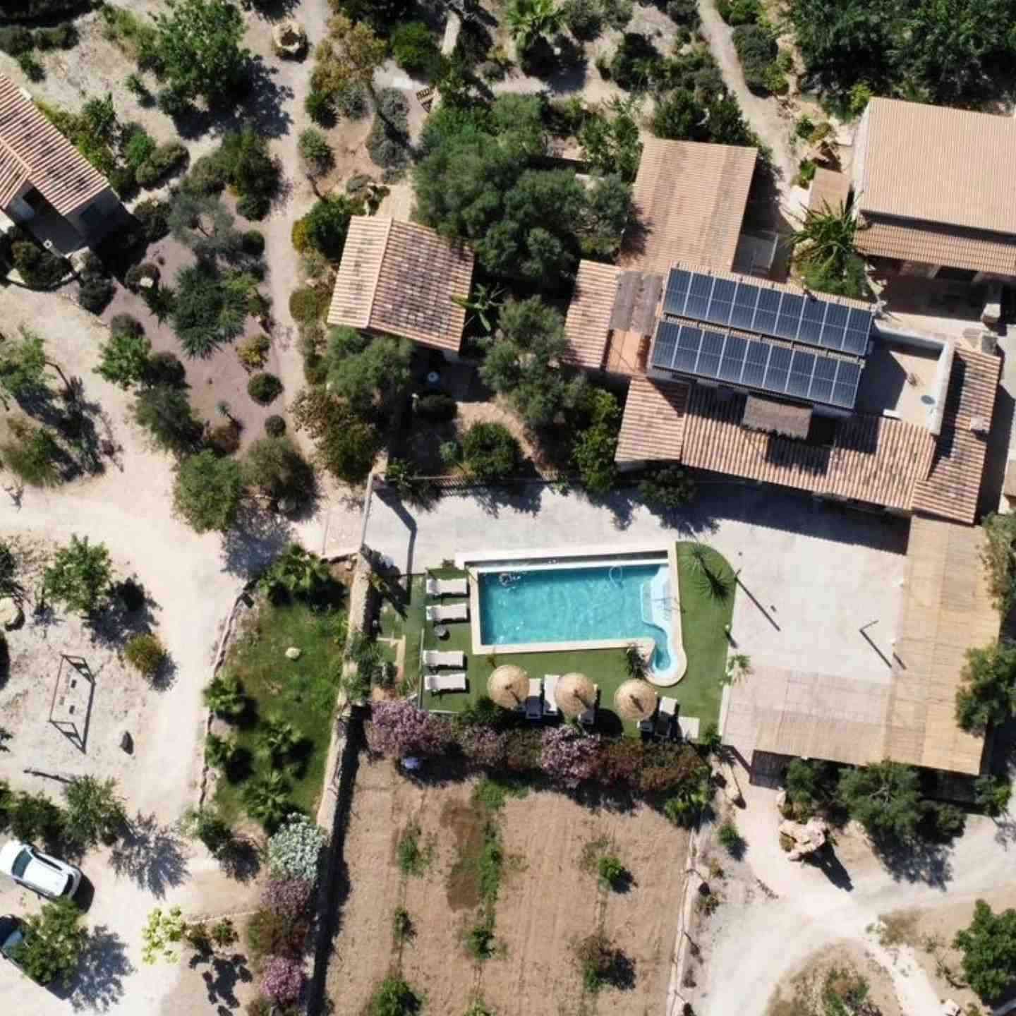 Vista aérea de una casa rural con piscina, paneles solares, árboles y parterres.