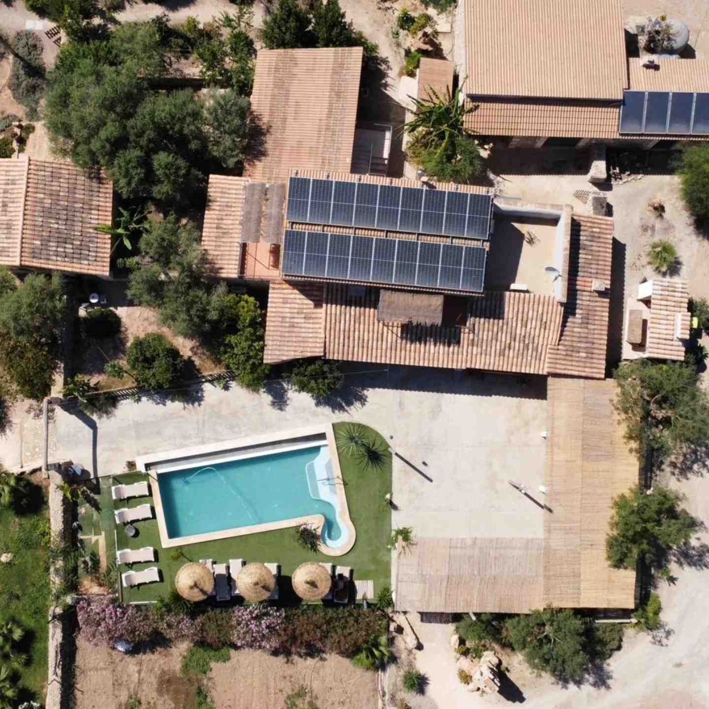 Vista aérea de una casa con paneles solares y una piscina en el patio trasero rodeada de árboles y áreas de patio.